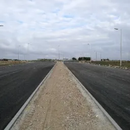 Nowa, dwupasmowa droga z pasem zieleni pośrodku, wykończona krawężnikami, oświetlona latarniami ulicznymi, pod pochmurnym niebem.