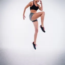 Kobieta w sportowym stroju wykonuje dynamiczne ćwiczenie unoszenia kolana w górę na jasnym tle.