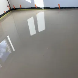 Świeżo wylana, samopoziomująca wylewka podłogowa w pomieszczeniu z zabezpieczonymi ścianami, widoczne odbicia okien.