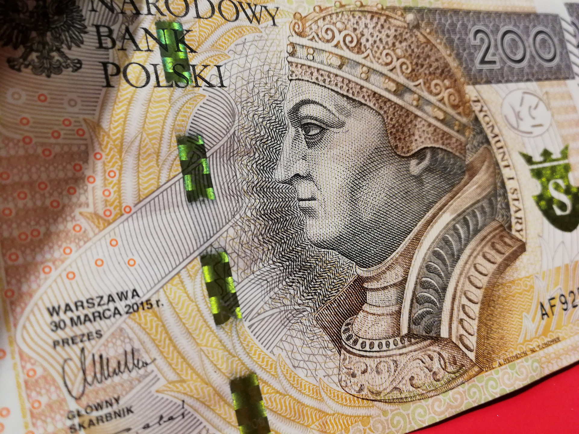 Zbliżenie na dwustuzłotowy banknot polski, ukazujący portret Zygmunta I Starego, hologramy i ornamenty.