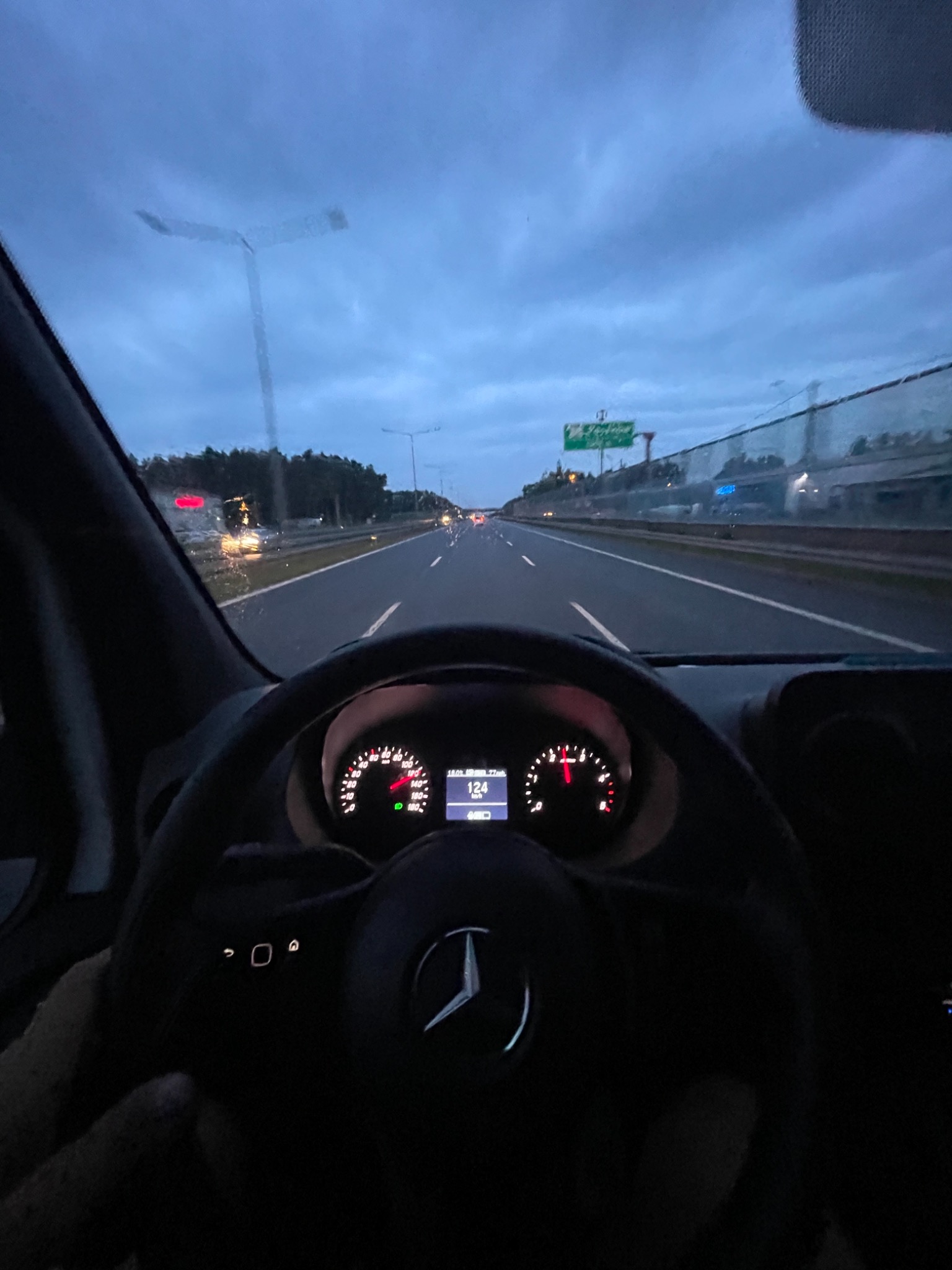 Widok z kabiny busa Mercedes-Benz Sprinter jadącego autostradą o zmierzchu, prędkościomierz wskazuje 124 km/h.