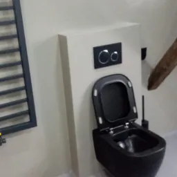 Czarna, wisząca toaleta z otwartą deską, zamontowana na stelażu podtynkowym w jasnej łazience, obok grzejnik drabinkowy.