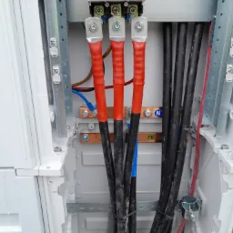 Wnętrze skrzynki elektrycznej z zamontowanymi przewodami oznaczonymi kolorowymi koszulkami termokurczliwymi, podłączonymi do listew zaciskowych i wyłącznika, widoczne oznaczenia na przewodach...