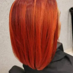 Krótkie, proste włosy w odcieniach intensywnej czerwieni i miedzi, z ciemniejszymi odrostami, widziane z tyłu, na tle jasnoszarej ściany.