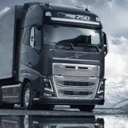 Czarny ciągnik siodłowy Volvo FH16 750 z naczepą, zaparkowany w Jarocinie z odbiciem w kałuży i górskim krajobrazem w tle.