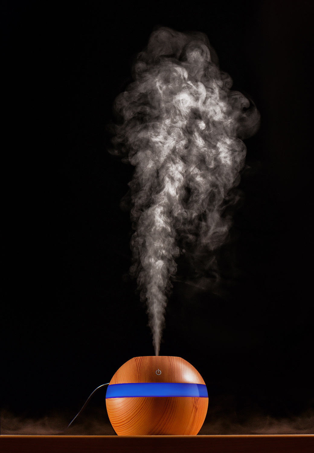Nawilżacz powietrza o drewnianej fakturze, z niebieskim podświetleniem, emituje strumień pary na czarnym tle.