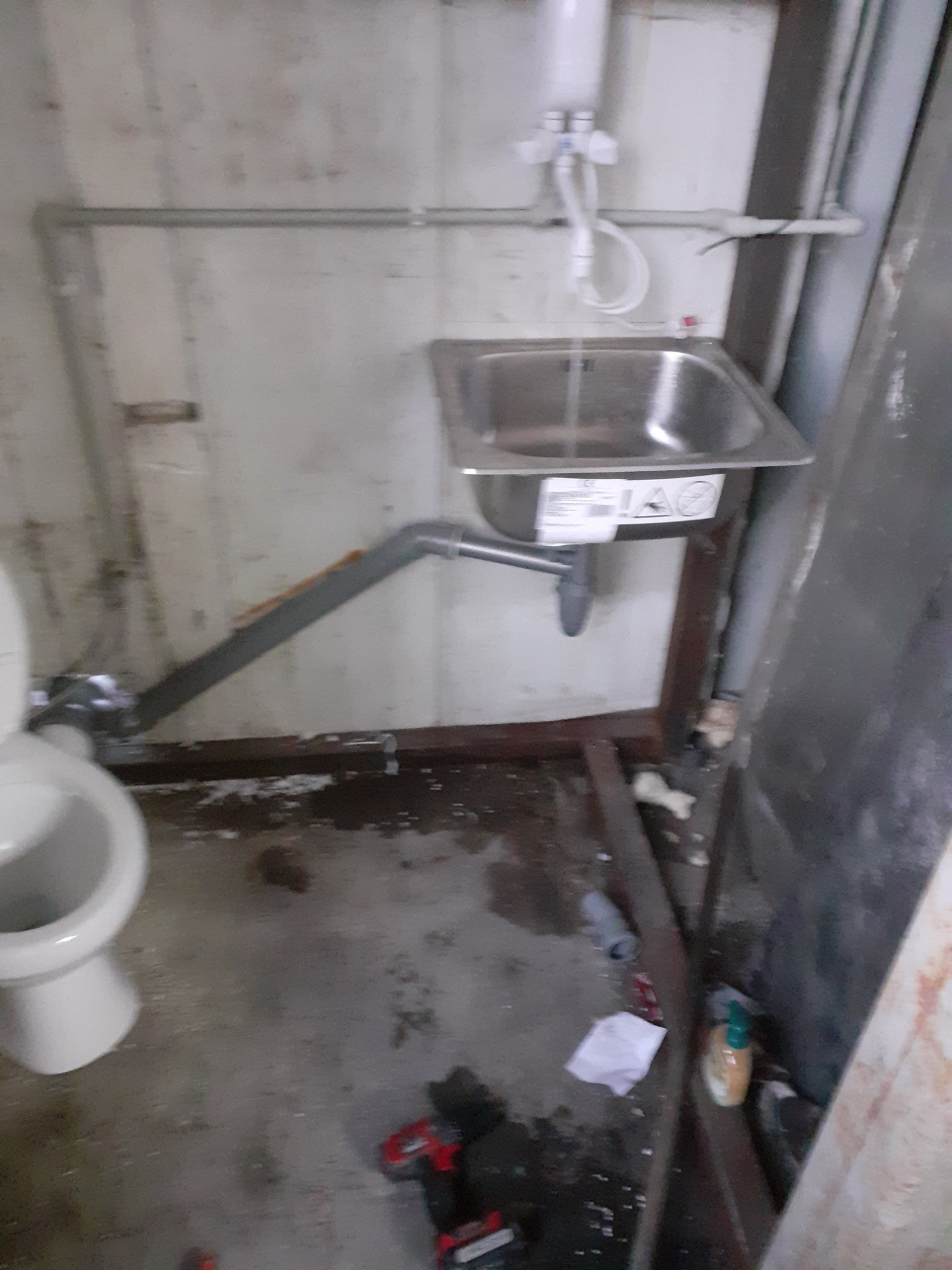 Niedokończona instalacja umywalki i toalety w pomieszczeniu z widocznymi śladami prac instalacyjnych, w tle białe ściany, na podłodze narzędzia i materiały budowlane.