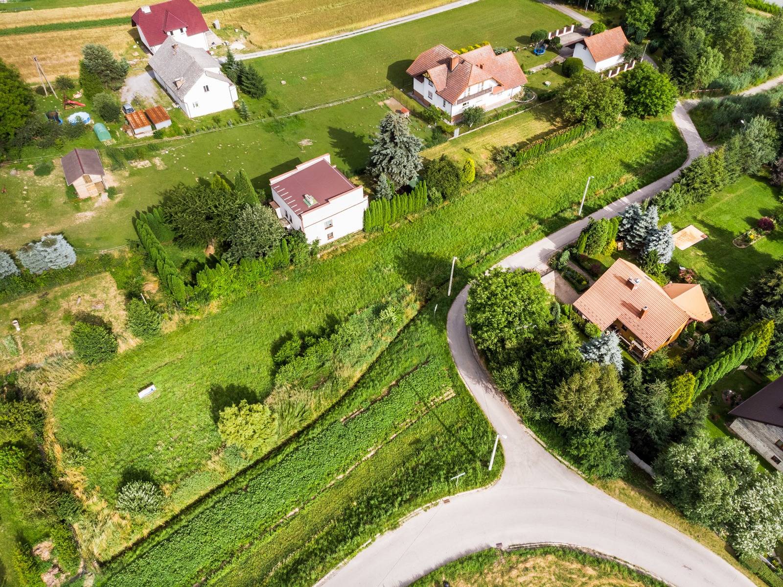 Widok z lotu ptaka na osiedle domów jednorodzinnych z ogrodami, zróżnicowana architektura i zieleń, słoneczny dzień.