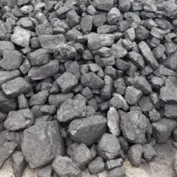 Stos szarego węgla kamiennego różnej wielkości, o nieregularnych kształtach, ułożony na szarym podłożu.