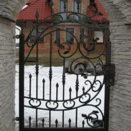 Kuta furtka z ozdobnymi elementami na tle domu z czerwonej cegły i śniegu.