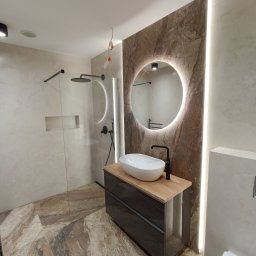 Kostrzewski - Nowoczesna łazienka z kabiną prysznicową typu walk-in, umywalką na szafce z drewnianym blatem i okrągłym lustrem z podświetleniem LED. Marmurowe płytki na podłodze i ścianie.