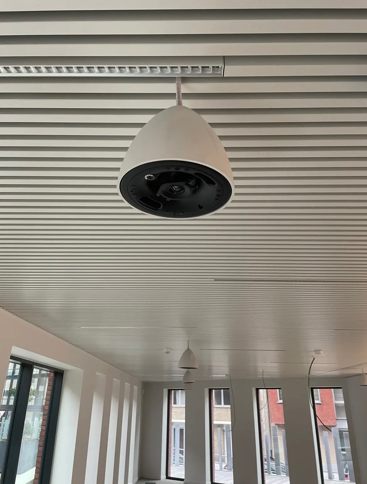 Nowoczesna, kulista lampa sufitowa w minimalistycznym biurze z żaluzjowym sufitem, widok z dołu na czarny element mocujący.