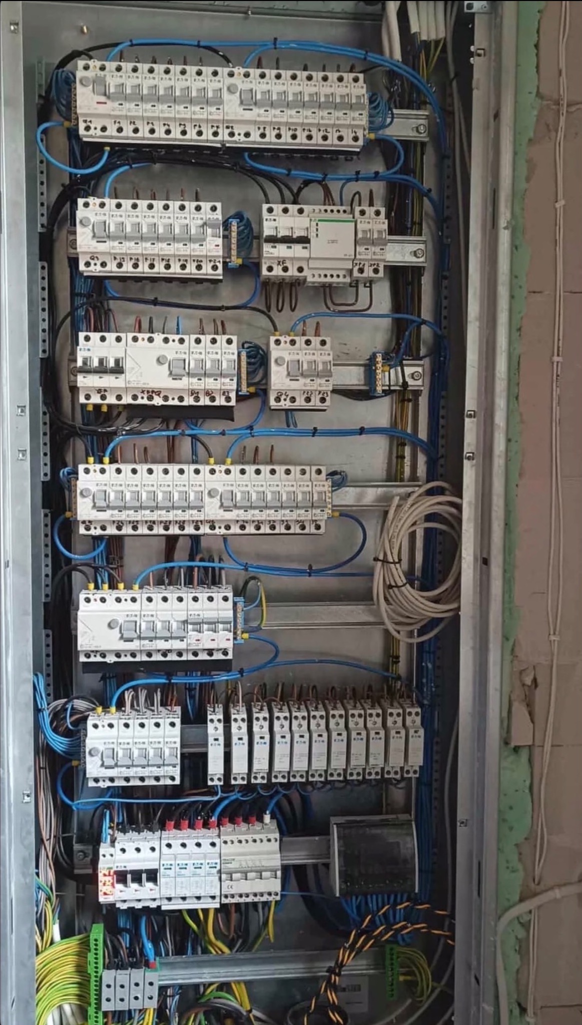 Rozdzielnica elektryczna z bezpiecznikami i okablowaniem w surowym wnętrzu. Widok na zamontowaną instalację przed wykończeniem ściany.