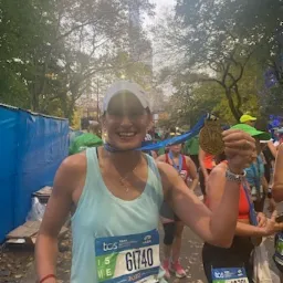 Uśmiechnięta kobieta z medalem na szyi i numerem startowym 61740, po ukończonym biegu maratońskim w plenerze miejskim.