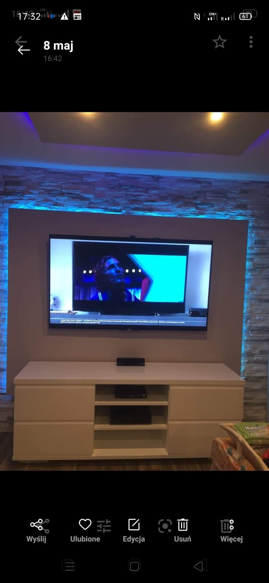 Salon z telewizorem na ścianie z dekoracyjną cegłą i podświetleniem LED, biała szafka RTV pod telewizorem.