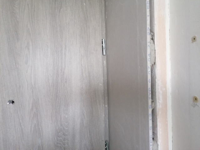 Fragment ściany z zamontowaną płytą kartonowo-gipsową, widoczne łączenia i ślady szpachlowania, surowe wykończenie.