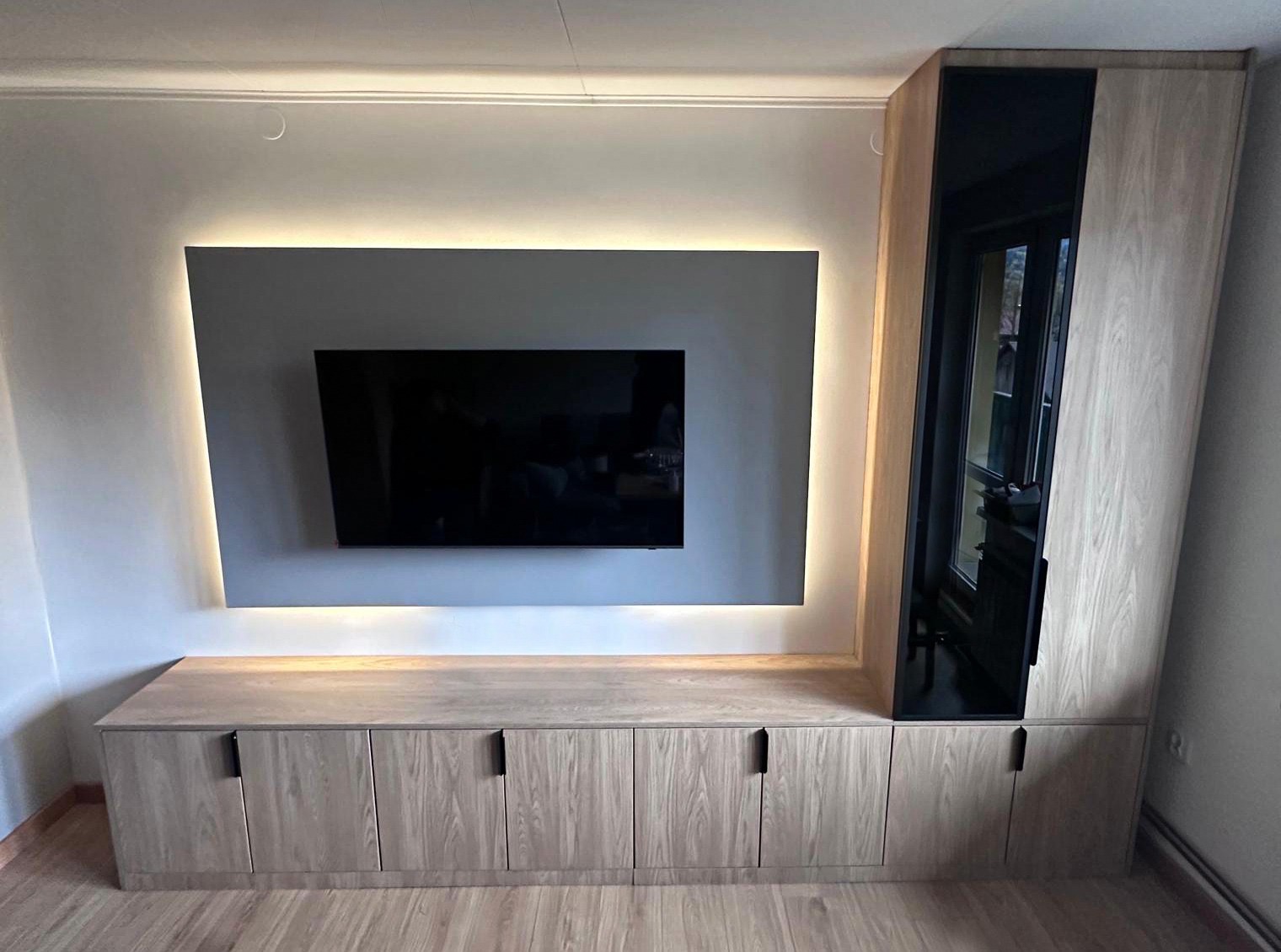 Szafka RTV na wymiar z oświetleniem LED w Zawoi. Jasne drewno, minimalistyczne uchwyty, czarna wstawka. Nowoczesny design, idealne dopasowanie do wnętrza.