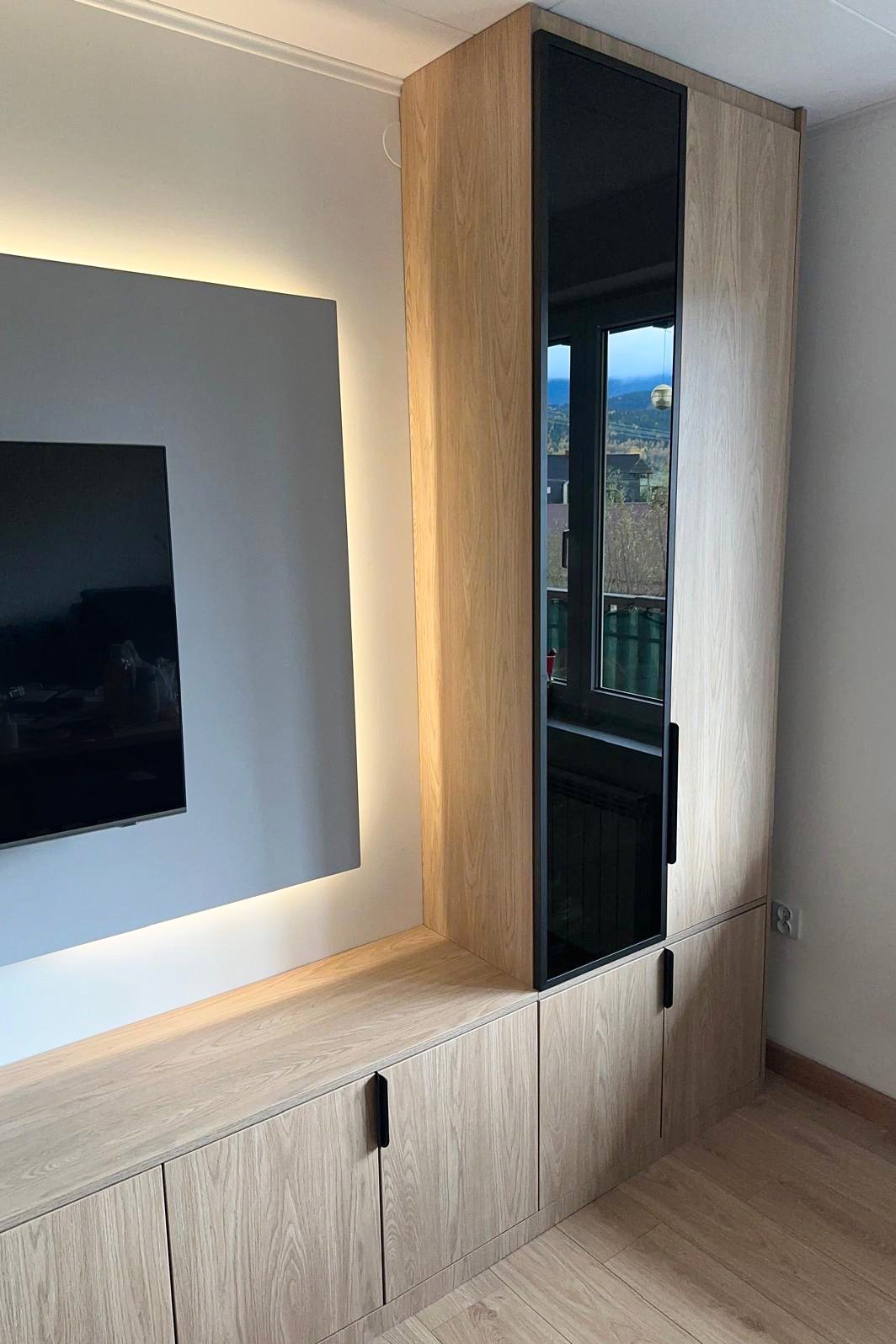 Jasna szafa z czarnym szkłem, wbudowana w ścianę z podświetleniem LED, minimalistyczny design, widok z boku, drewnopodobne wykończenie, czarne uchwyty.