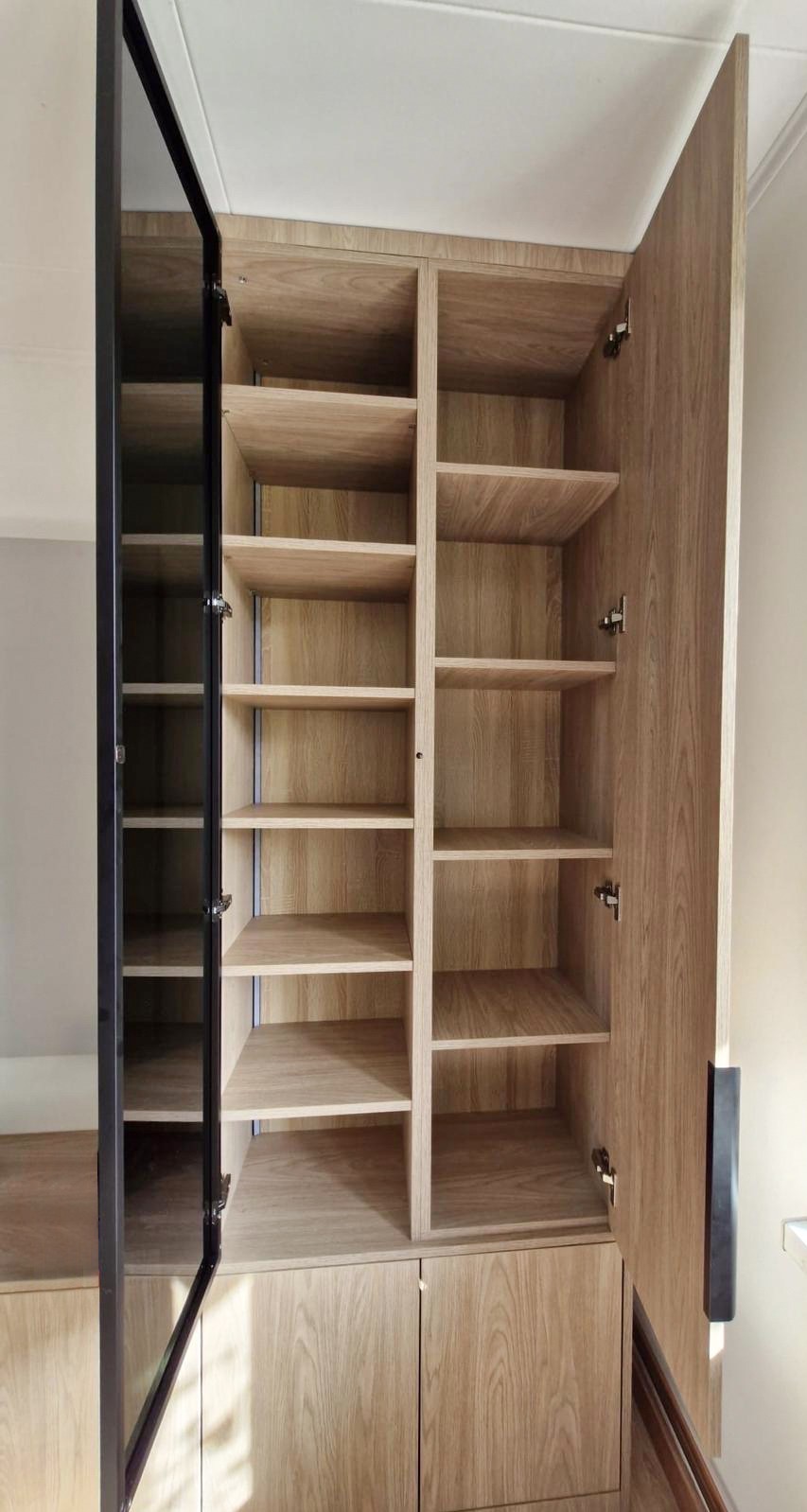 Jasna szafa z otwartymi drzwiami, widoczne półki. Jedne drzwi z czarną ramą i szkłem. Drewnopodobne wykończenie. Nowoczesny design.