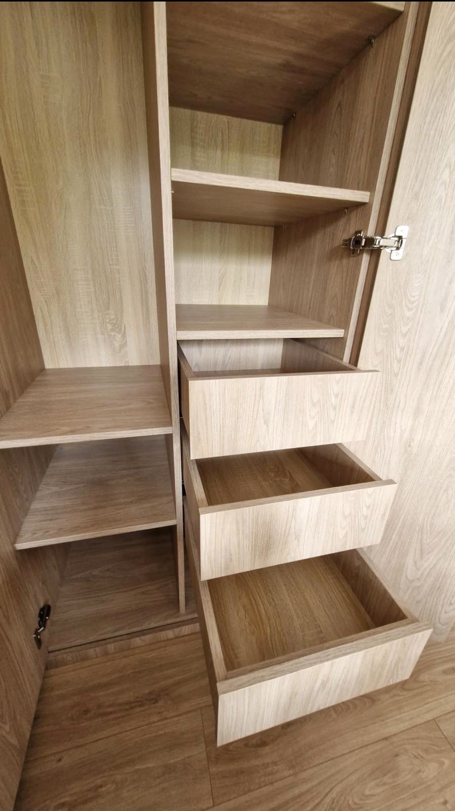 Jasna, drewniana szafa z otwartymi półkami i dwoma wysuniętymi szufladami, ukazująca wnętrze i strukturę mebla. Widoczne detale wykończenia i okucia.