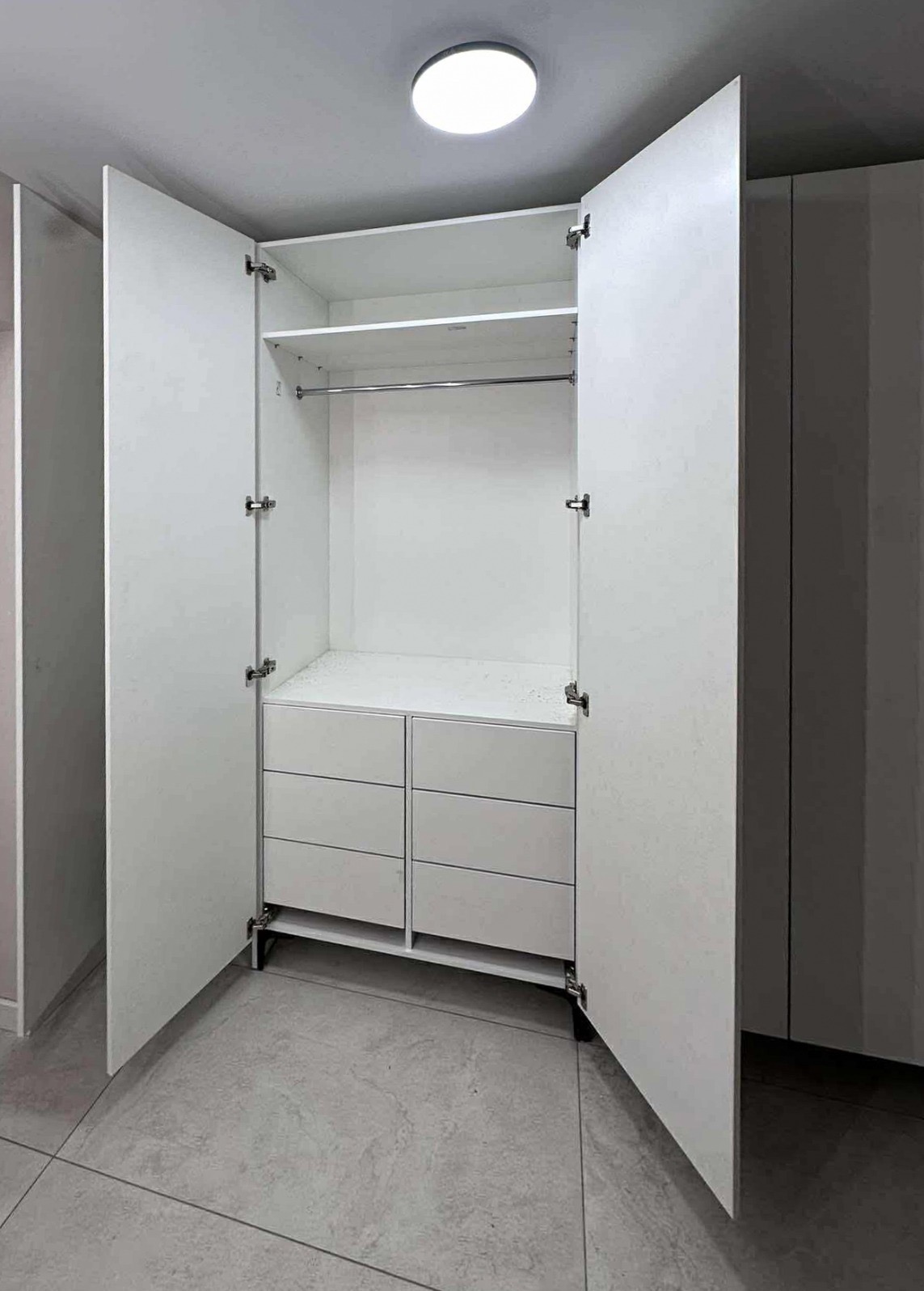 Wnętrze białej, otwartej szafy z szufladami i drążkiem na ubrania, widok z dołu, minimalistyczny design, oświetlenie sufitowe.