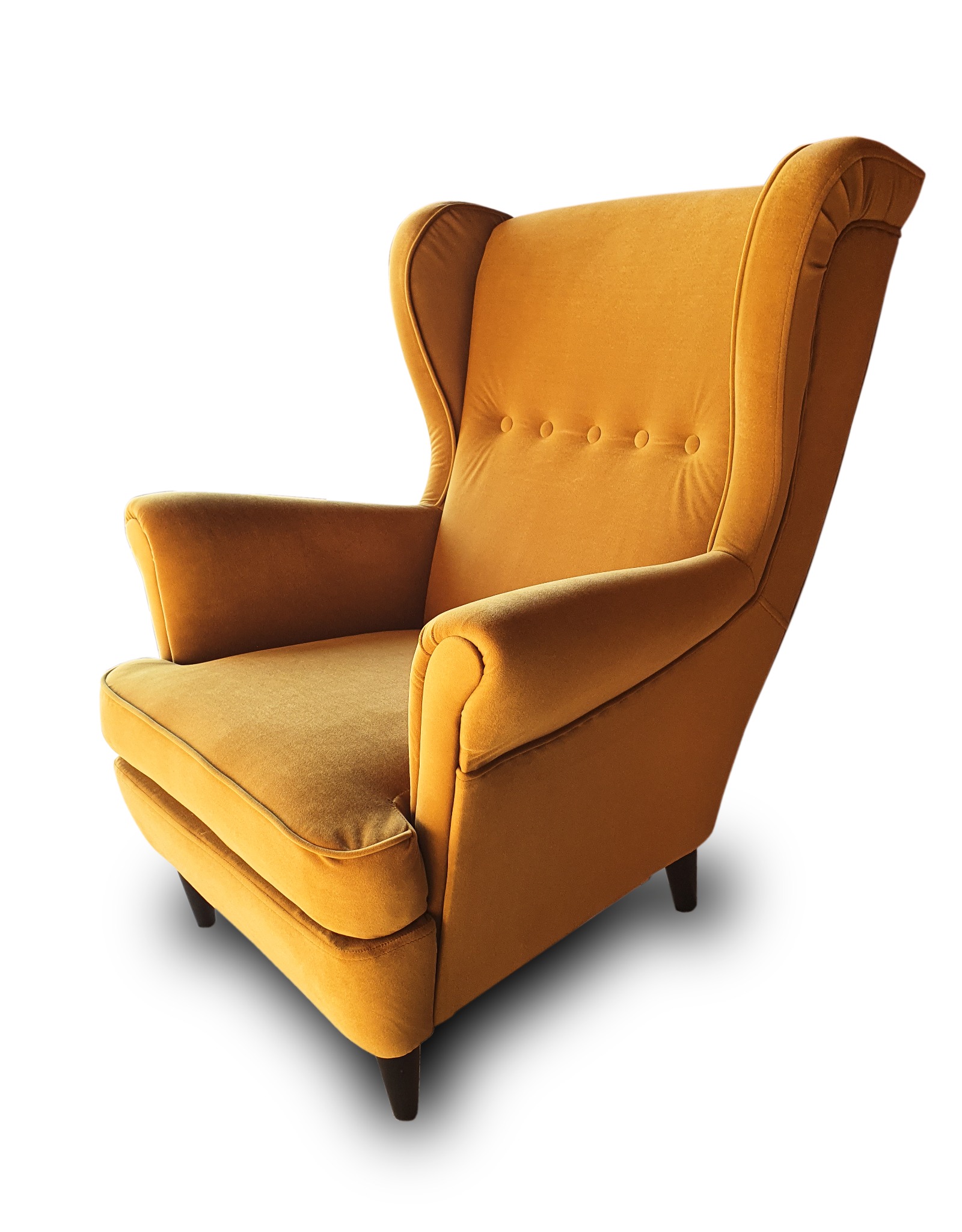 Musztardowy fotel uszak z guzikami na oparciu, na krótkich, ciemnych nóżkach, sfotografowany na białym tle.