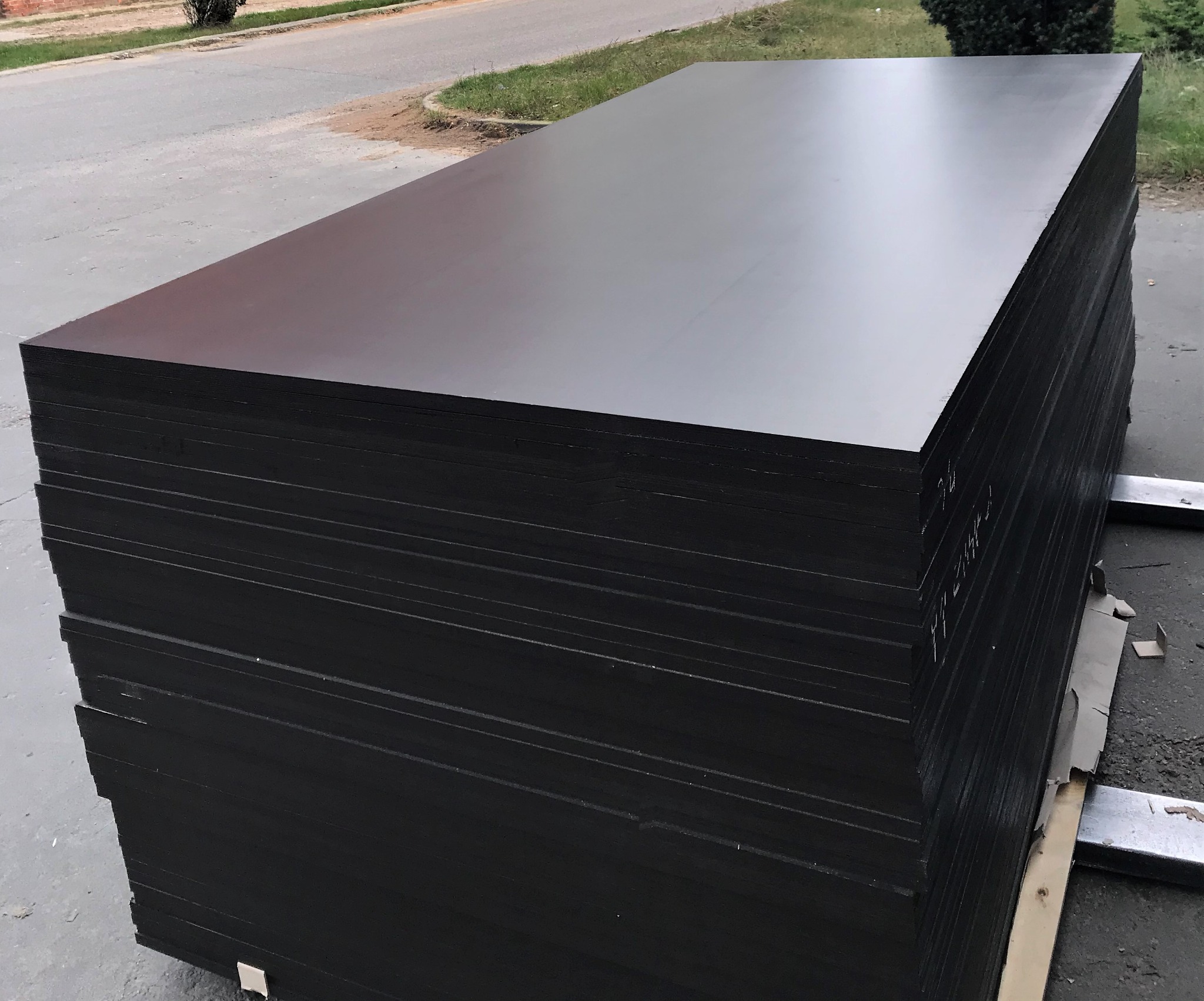 Stos czarnych, lakierowanych płyt szalunkowych ułożonych na palecie na zewnątrz, widoczne białe napisy na boku stosu.