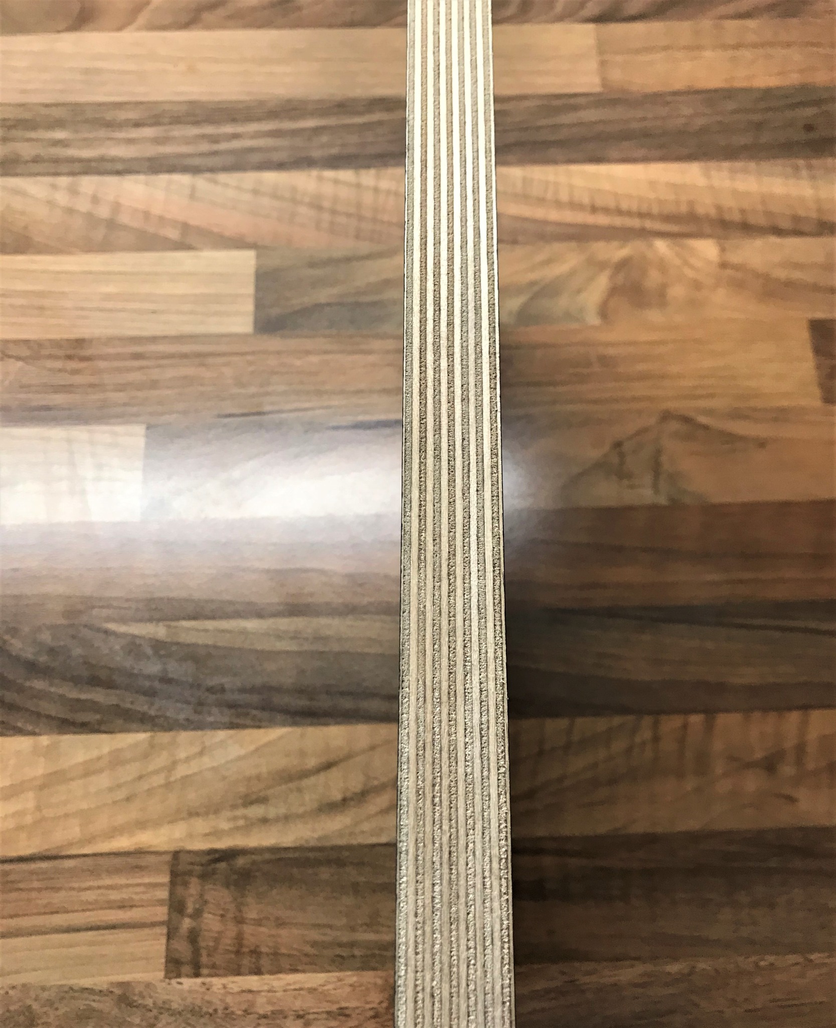 Przekrój poprzeczny płyty drewnianej z widoczną strukturą warstwową na tle drewnopodobnej powierzchni.