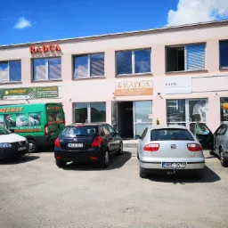 Budynek biura rachunkowego RADCA z zaparkowanymi samochodami na parkingu w słoneczny dzień. Widoczny szyld z danymi kontaktowymi i logo firmy.