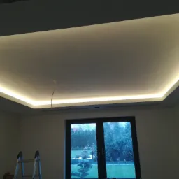 Nowoczesny sufit podwieszany z oświetleniem LED, widoczna drabina malarska i okno z widokiem na ogród