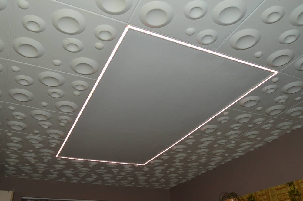 Dekoracyjny sufit z panelami 3D i wpuszczonym prostokątnym oświetleniem LED, tworzącym efektowną ramę świetlną.