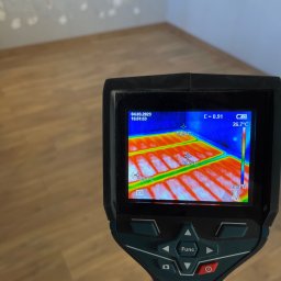 HEAT AT HOME SP. Z O.O. - Pomiar temperatury podłogi za pomocą kamery termowizyjnej; widoczne rozłożenie ciepła w instalacji, ściana z widocznymi śladami po remoncie.