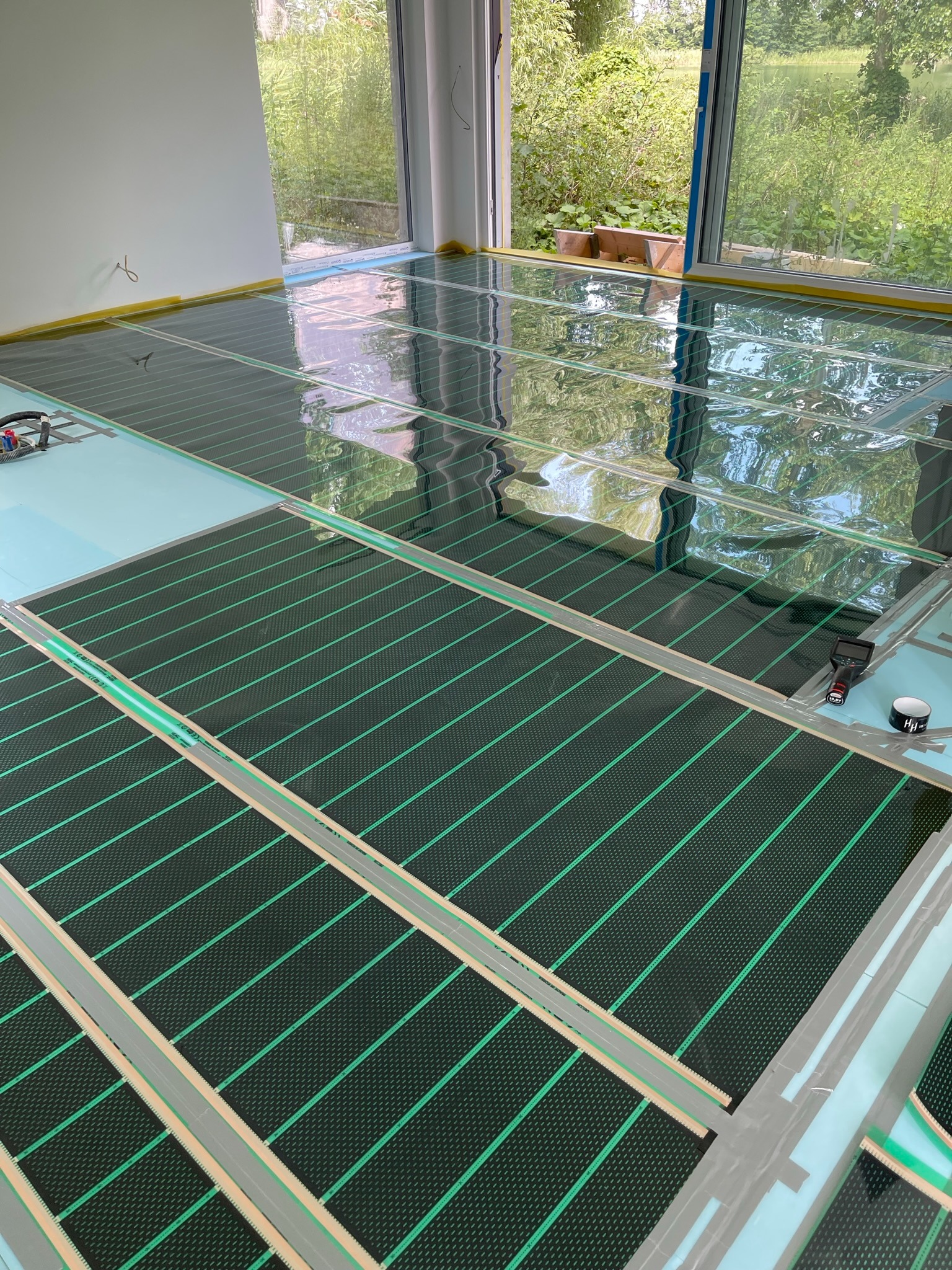 Montaż maty grzewczej na podłodze z widocznym oknem na zewnątrz i folią ochronną na części powierzchni.