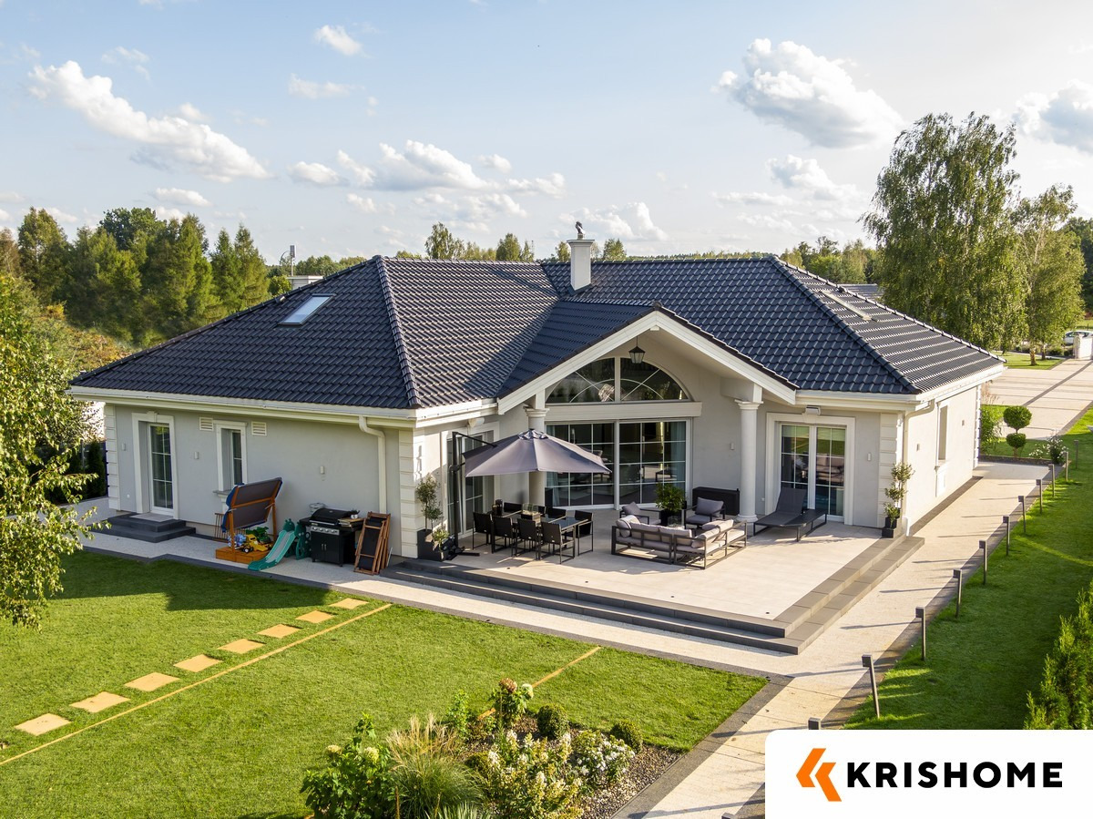 Elegancki dom jednorodzinny z tarasem i dużymi oknami, widok z góry. Na dachu widoczny komin z ozdobną figurką. Uwagę przykuwają przesuwne okna tarasowe.