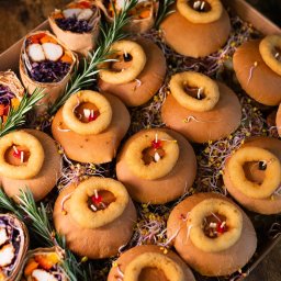 Top Party Box Sp. z o.o. - Box cateringowy: tortille z warzywami i kurczakiem oraz mini burgery z krążkami cebulowymi, dekorowane rozmarynem i kiełkami, na drewnianym tle.