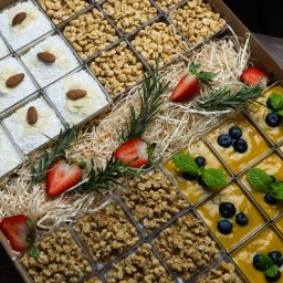 Top Party Box Sp. z o.o. - Catering w boxach: pudełko z przegródkami, w których znajdują się desery (kokosowe, z mango i borówkami, granola, prażony ryż) udekorowane owocami i rozmarynem.