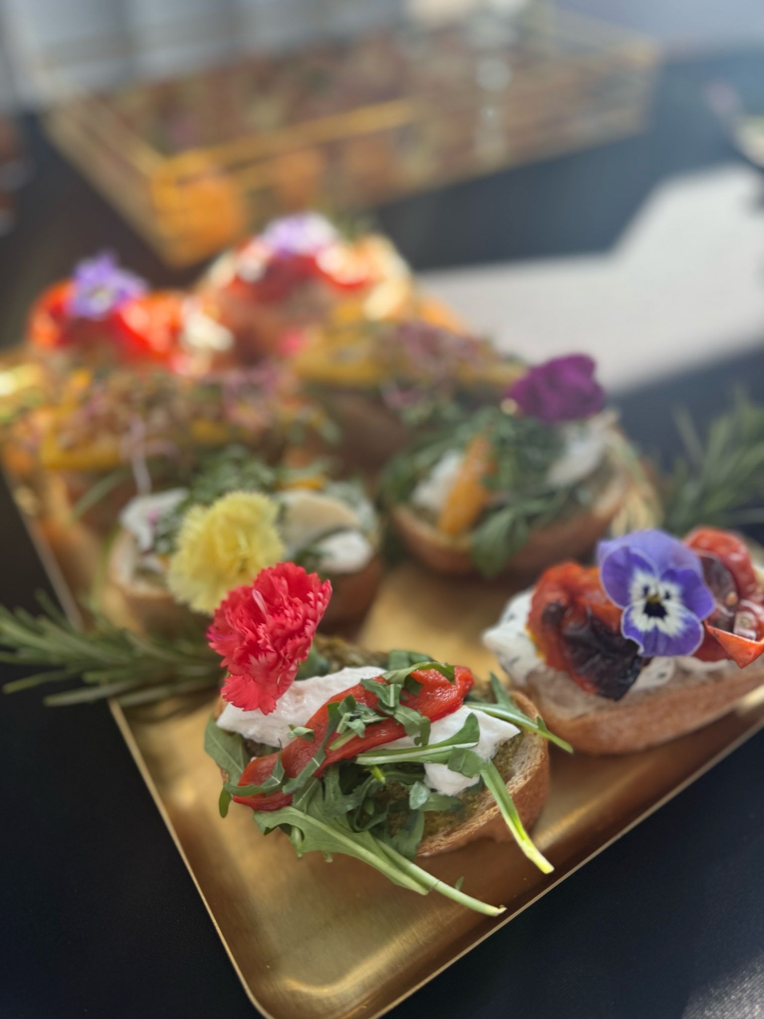 Dekoracyjne kanapeczki na złotej tacy, z kwiatami i świeżymi warzywami, idealne na catering w Poznaniu. Elegancka prezentacja oferty Luxury.