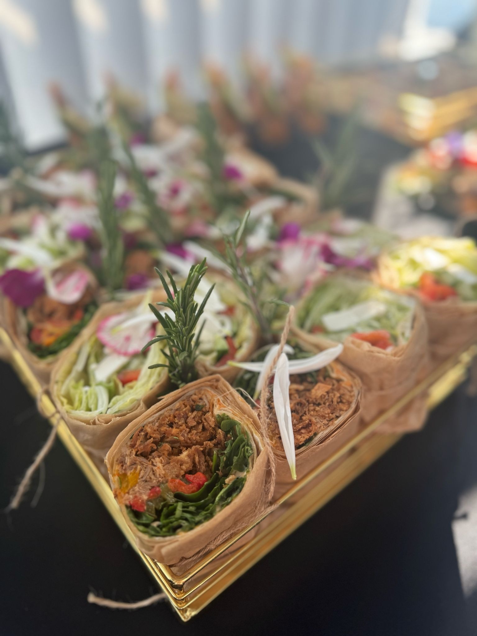 Elegancki catering: Wrapy z warzywami i mięsem, udekorowane rozmarynem i kwiatami, ułożone na złotej tacy. Luksusowa oferta.