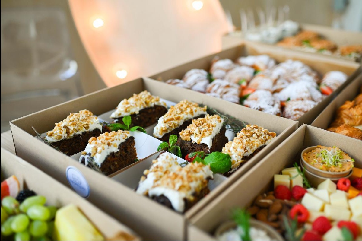 Boxy cateringowe z deserami, ciastami i przekąskami, widoczne z góry, w naturalnym oświetleniu. Różnorodność słodkich i słonych propozycji.
