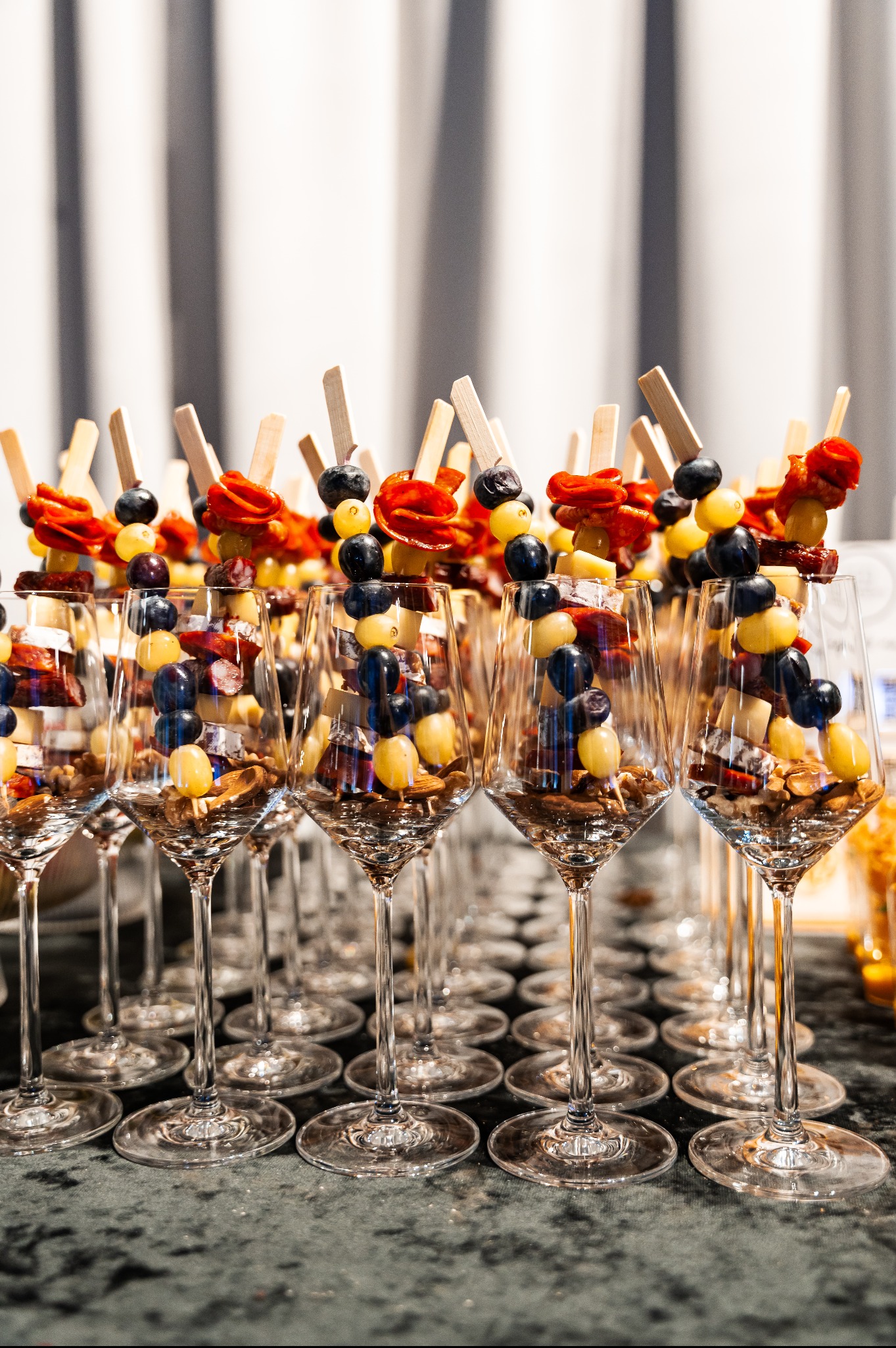 Elegancki catering: kieliszki wypełnione orzechami, serem, winogronami i salami na szpadkach. Idealne na event firmowy lub pokaz mody. Stonowana kolorystyka.