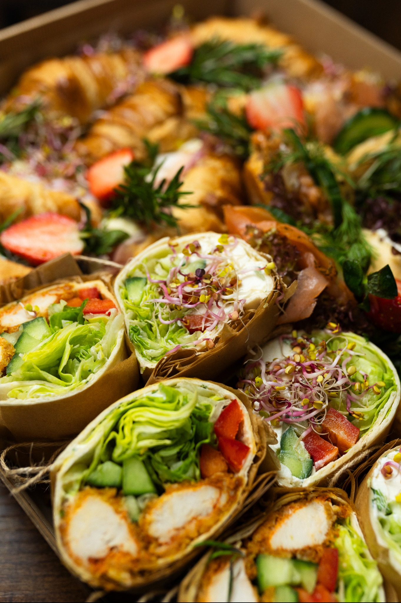 Box cateringowy z wrapami i croissantami, udekorowany świeżymi ziołami i truskawkami. Elegancki zestaw lunchowy z dostawą w Poznaniu.