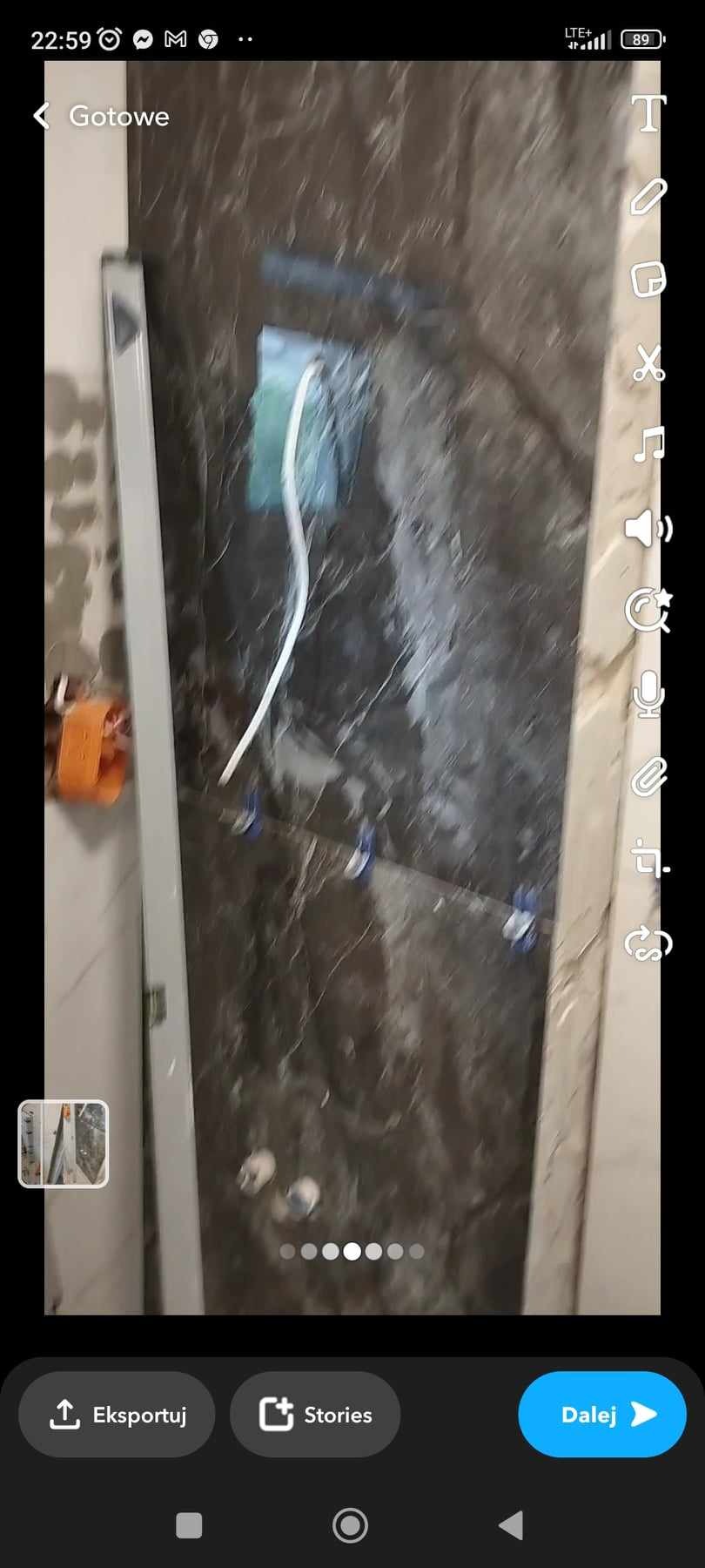 Ściana łazienki wyłożona ciemnymi płytkami imitującymi marmur, z widocznymi krzyżykami dystansowymi i wystającą rurką instalacji wodnej.