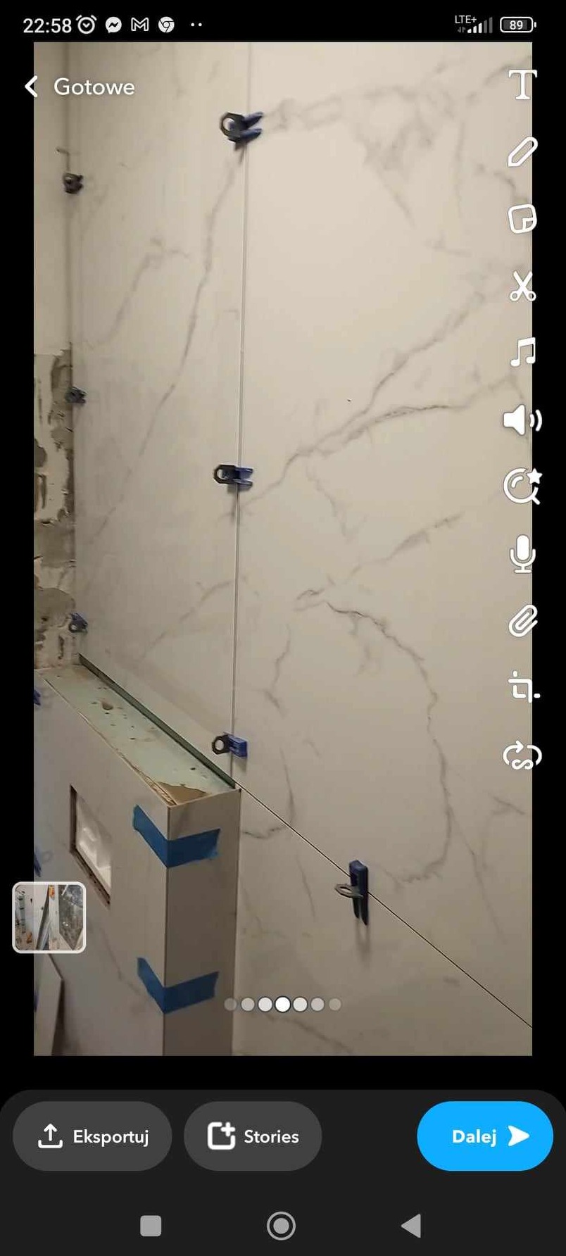 Układanie płytek imitujących marmur na ścianie w łazience z użyciem systemu poziomowania płytek, widoczne niedokończone fragmenty ściany i obudowa wanny.