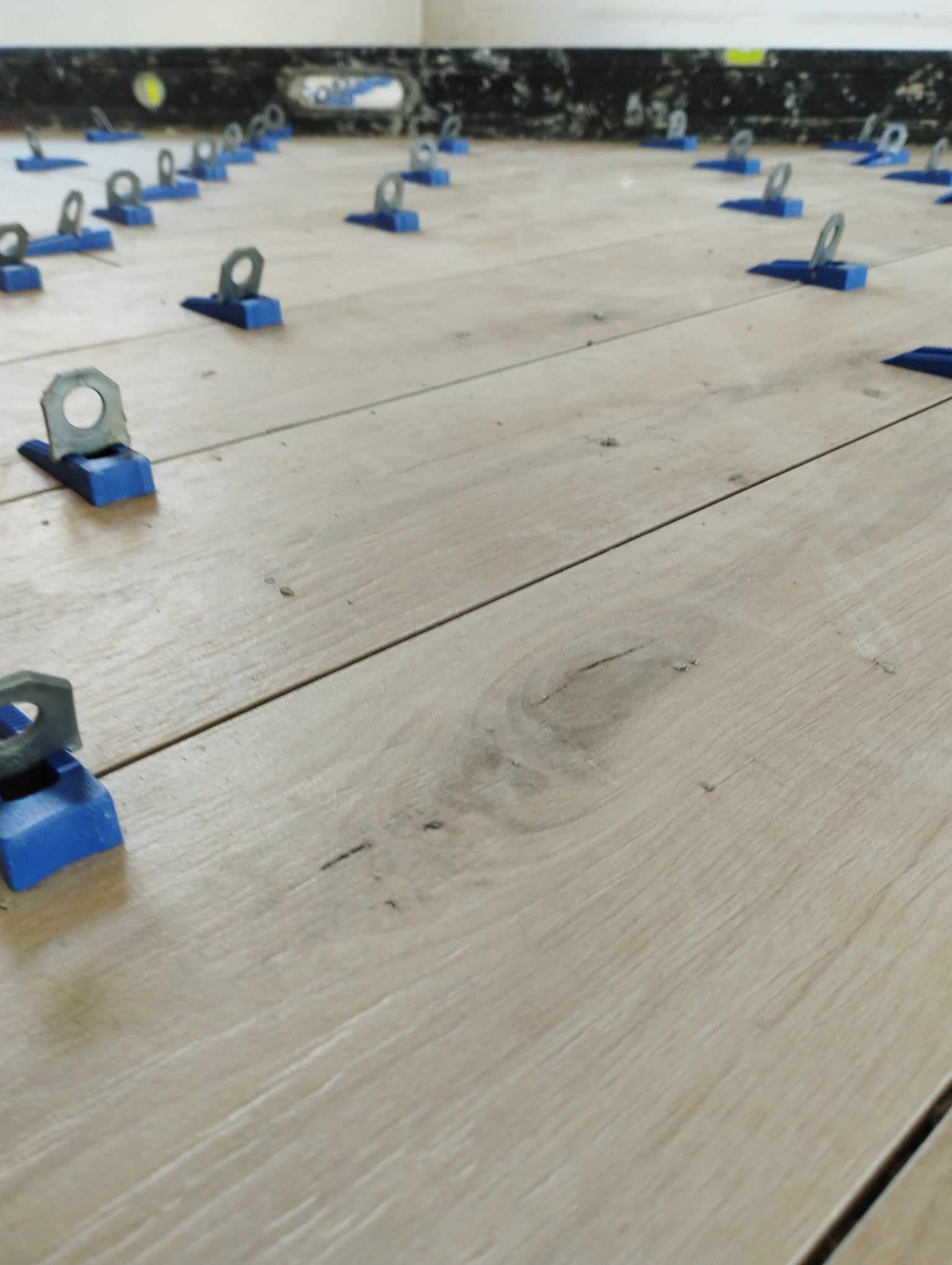 Ułożone panele podłogowe z systemem poziomowania, widoczne niebieskie klipsy i metalowe kliny.