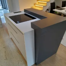 Nowoczesna wyspa kuchenna z szarym blatem i płytą indukcyjną, na tle schodów z podświetleniem LED.