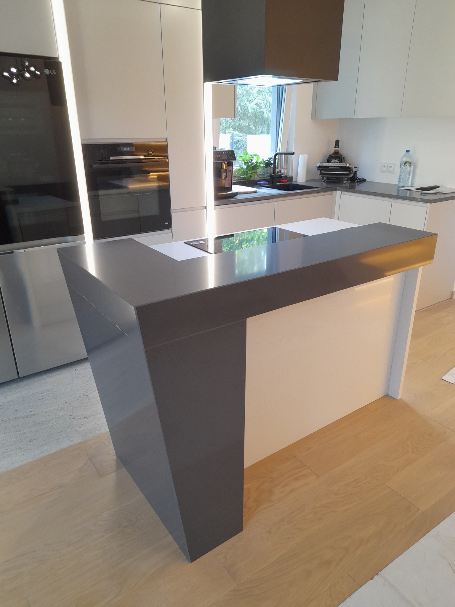 Szary blat wyspy kuchennej z oświetleniem LED od spodu, w nowoczesnej kuchni z białymi szafkami i drewnianą podłogą.