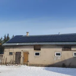 Instalacja paneli słonecznych na dachu budynku gospodarczego w Kolnie, widok na część ekipy montażowej i ośnieżone podwórze.