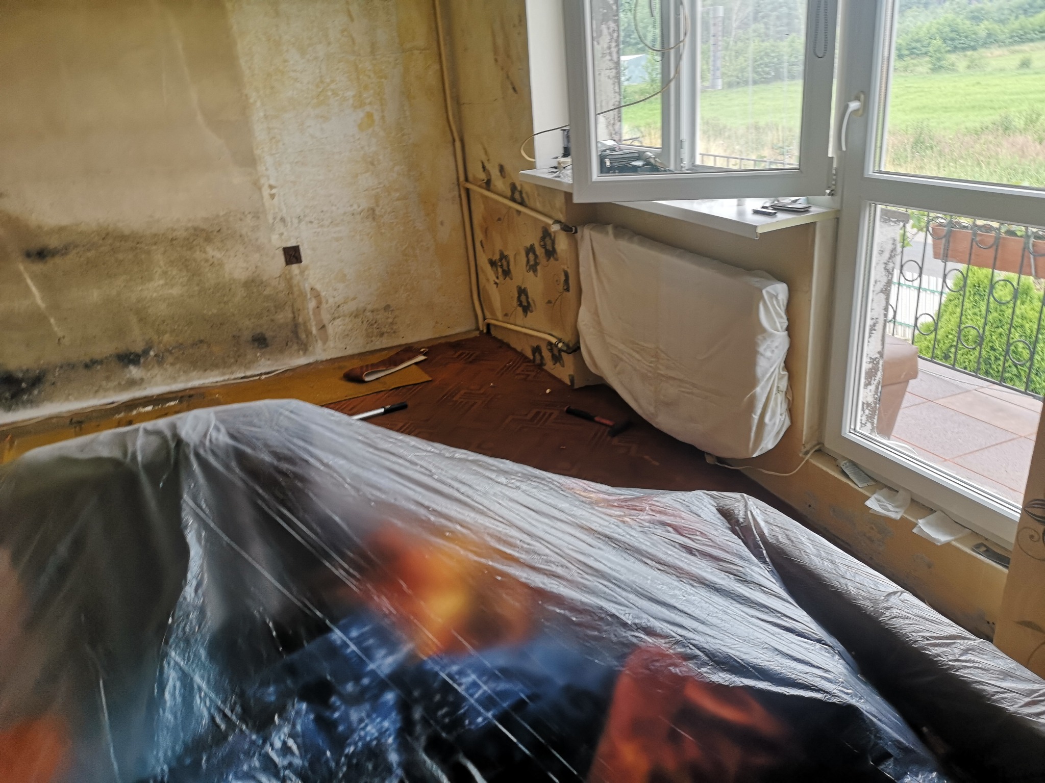 Pokój w trakcie przygotowań do prac remontowych: meble przykryte folią ochronną, ściany przygotowane do szpachlowania, widoczne narzędzia na podłodze.