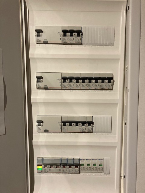 Rozdzielnia elektryczna z widocznymi bezpiecznikami, niektóre w pozycji włączonej, jeden z zieloną diodą sygnalizacyjną