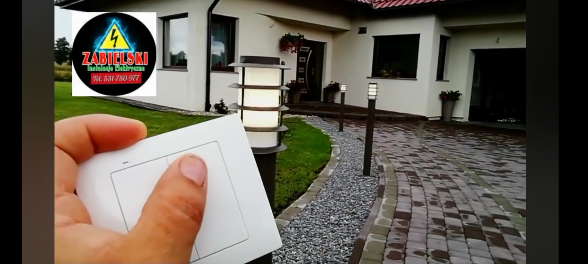 Sterowanie oświetleniem zewnętrznym domu za pomocą panelu dotykowego, widoczne nowoczesne lampy ogrodowe wzdłuż ścieżki.